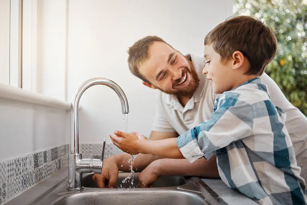 Father helping son wash his hands in the kitchen sink in Houston, TX.