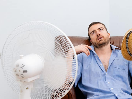 man sitting in front of fan because ac isn't working