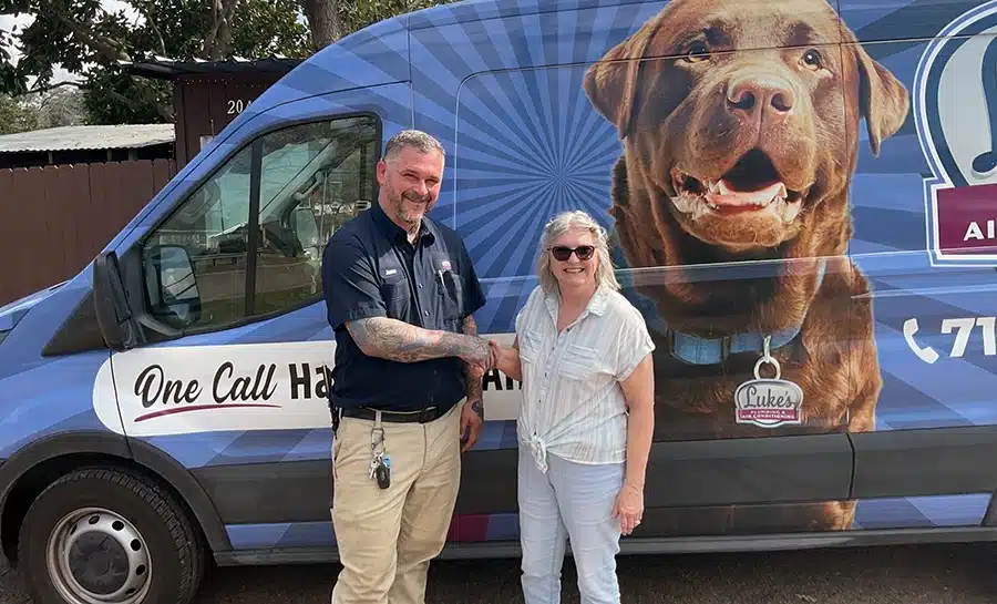 A Luke's Plumbing & Air technician shaking hands with a happy Houston customer in front of the branded service van