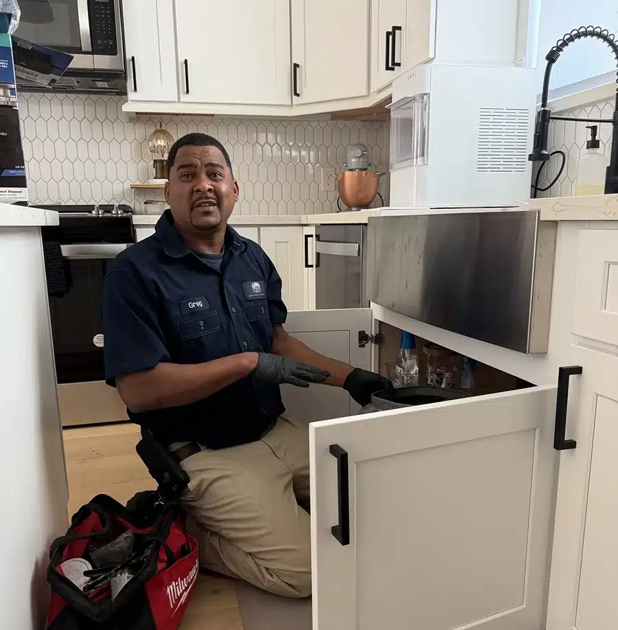 Greg from Luke's Plumbing on the job — installing garbage disposal under kitchen sink in a Houston home